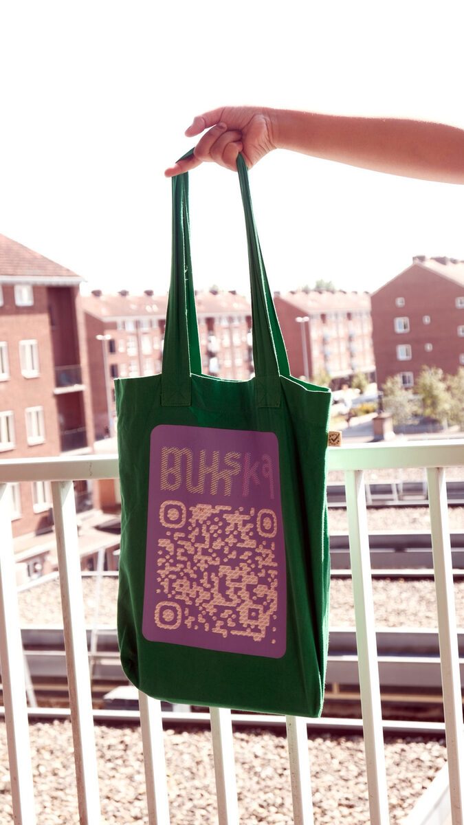 green muskabun tote bag held up on a balcony